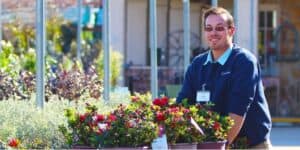 Bright smiling inventory specialist working with potted flowering plants at a nursery or garden center, emphasizing inventory management and horticulture expertise.