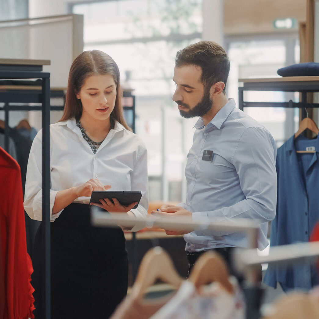 Retail clothing store inventory management, apparel inventory specialists, salesperson consulting with customer.