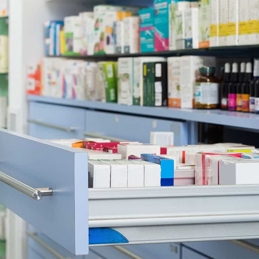 Prescription medication inventory on pharmacy shelves with organized drug boxes and bottles.