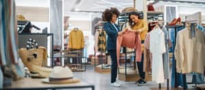 Stylish shoppers examining sweaters and clothing in a modern retail store, emphasizing inventory management, fashion retail, and shopping experience.