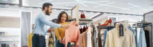 Customized clothing store shoppers examining fashion items on racks in a retail store.